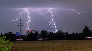Blitze eines Gewitters sind am späten Abend am Himmel hinter einer Stromleitung zu sehen.