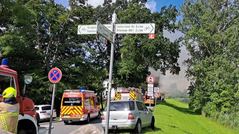 Feuerwehrauto stehen auf einer Straße im Blockland, im Hintergrund ist Rauch zu sehen.