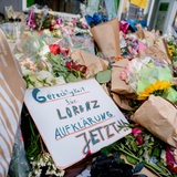 Blumen liegen auf einer Straße. Auf einem Schildchen steht "Gerechtigkeit für Lorenz".