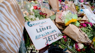 Blumen liegen auf einer Straße. Auf einem Schildchen steht "Gerechtigkeit für Lorenz".