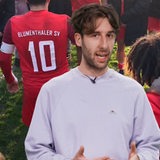 Ein junger Mann steht vor einem Bild, auf dem Fußballer zu sehen sind