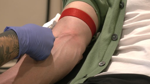 Eine Nadel wird in einen Arm gestochen um Blut zu spenden.