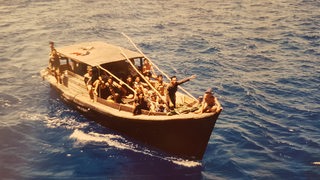 Ein Holzboot mit Menschen fährt über das Meer
