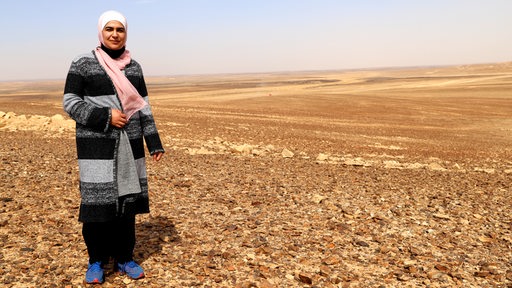 Eine Frau mit Kopftuch steht in einer Wüstenlandschaft
