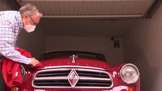 Ein Mann poliert einen roten Oldtimer in einer Garage.