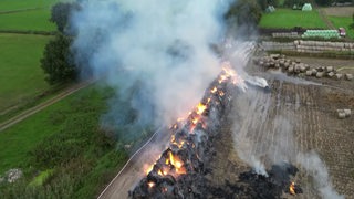 Auf einem Feld bei Bremen-Borgfeld brennen zahlreiche Heuballen.
