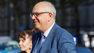 Ein Mann mit Brille und Anzug lächelt.