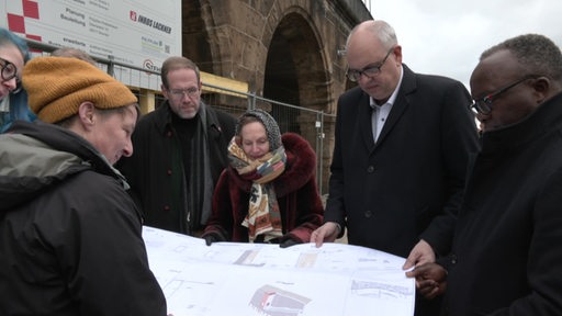 Der Mahnmal-Bau zum gedenken an die Juden an der Weser beginnt. Bürgermeister Bovenschulte hält den Bauplan zusammen mit anderen Personen in den Händen.
