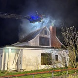 Eine Drehleiter mit Einsatzkraft ragt an ein verrauchtes Haus heran.
