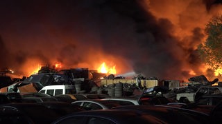 Ein Feuer wütet hinter Autos auf einem Recyclinghof.