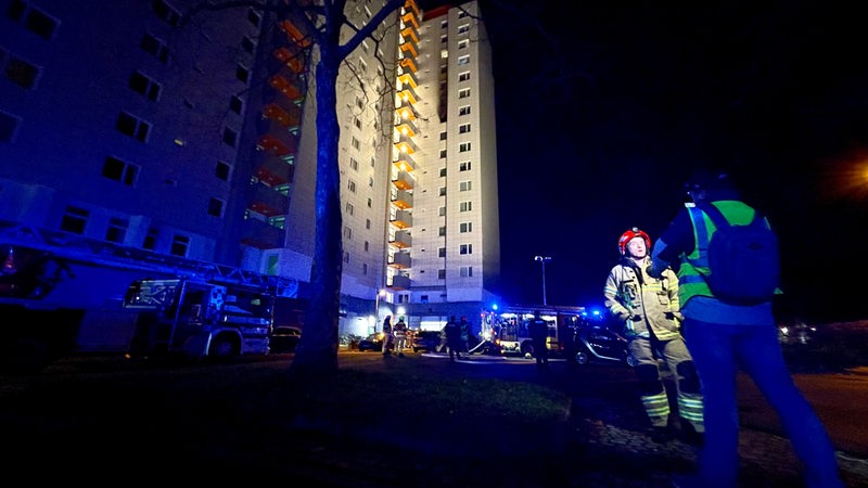 Feuerwehrwagen stehen nachts mit Blaulicht vor einem Hochhaus