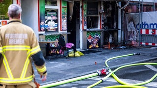 Ein Feuerwehrmann der Feuerwehr Bremen steht vor einem ausgebrannten Döner-Imbiss