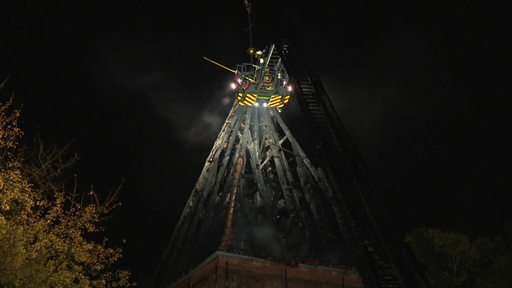 Ein ausgebrannter Kirchturm wird von Feuerwehrleuten gelöscht.