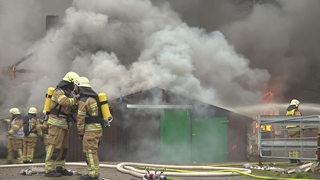 Feuerwehrleute stehen in voller Montur vor einer brennenden Scheune