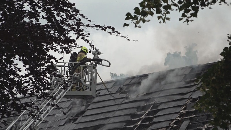 Ein Feuerwehrmann auf einer Leiter löscht einen Brand in einem Dach.