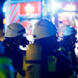 Feuerwehrleute stehen in Arbeitskleidung vor einem Feuerwehrauto.