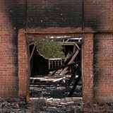 Durch ein Loch in der Wand ist ein Gebäude zu sehen, das durch einen Brand zerstört wurde