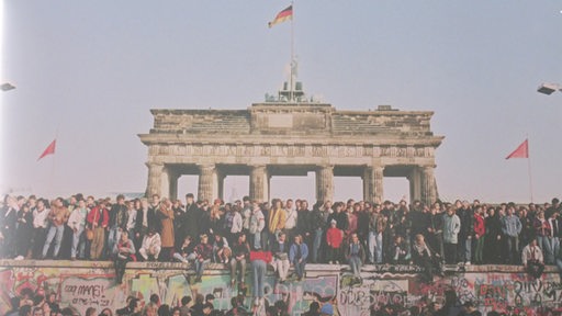 Unzählige Menschen stehen vor und auf der Berliner Mauer vor dem Brandenburger Tor während des Mauerfalles