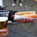 Eine Person hält einen Bierbecher und eine Bratwurst in den Händen