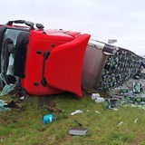 Ein von Bierkisten und zerbrochenen Flaschen umgebener Lkw liegt umgekippt neben einer Autobahnabfahrt.