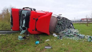 Ein von Bierkisten und zerbrochenen Flaschen umgebener Lkw liegt umgekippt neben einer Autobahnabfahrt.