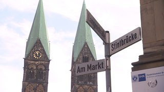 Mehrere Straßennamen-Schilder mit dem Bremer Dom im Hintergrund. 