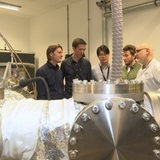 Fünf Weltraum-Forscher stehen um einen Teilchenbeschleuniger herum