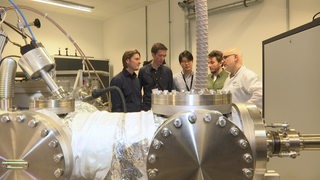 Fünf Weltraum-Forscher stehen um einen Teilchenbeschleuniger herum