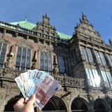 Hinter einem Geldscheinfächer ist das Rathaus von Bremen zu sehen. 