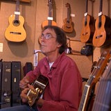 Ein Mann spielt Gitarre. Um ihn herum sind viele weitere Gitarren zu sehen.