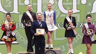 Die Irish Dance-Tänzerin Svenja Stolz steht auf einem Podest und bekommt eine Urkunde überreicht.