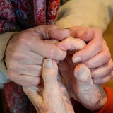 Hände einer alten Frau werden gehalten.