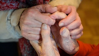 Hände einer alten Frau werden gehalten.