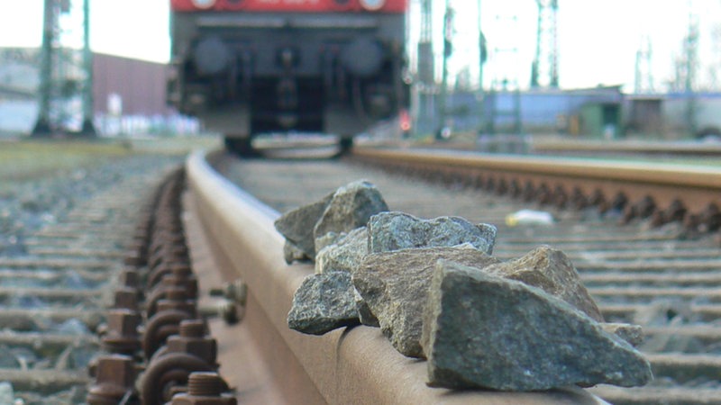 Während sich ein Zug nähert, liegen auf einem Bahngleis mehrere Steine.