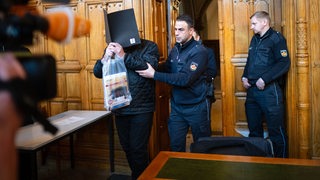 Ein Angeklagter wird vor Prozessbeginn in einen Gerichtssaal geführt. 