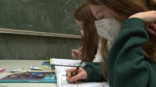 Zwei Schülerinnen sitzen vor einem Lehrbuch.