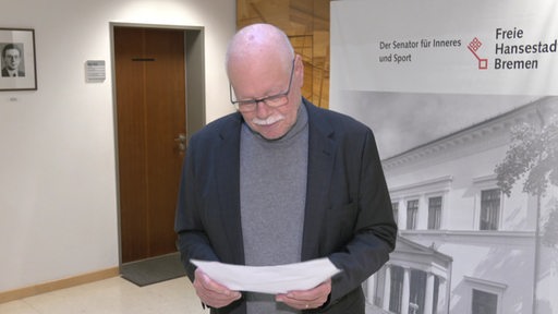 Der Innensenator Ulrich Mäurer liest etwas auf einem Zettel. 