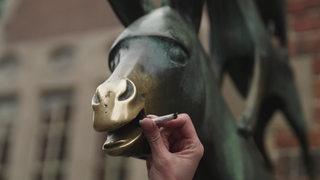Eine Zigarette wird an die Schnauze des Esels an der Statue der Bremer Stadtmusikanten gehalten.