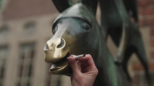 Eine Zigarette wird an die Schnauze des Esels an der Statue der Bremer Stadtmusikanten gehalten.