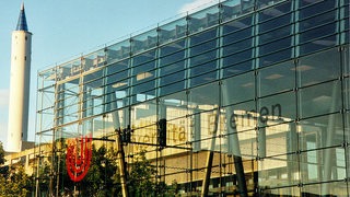ein großer Bau aus Glas, im HIntergrund der Fallturm