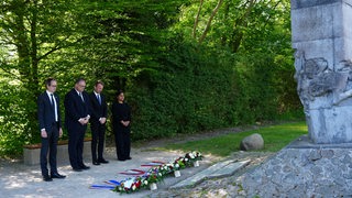 Vor dem Denkmal am U-Boot-Bunker Valentin stehen drei Frauen und ein Mann und gedenken vor niedergelegten Kränzen.