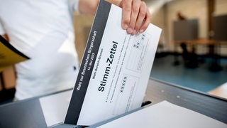 Eine Frau wirft einen Stimmzettel in eine Wahlurne.