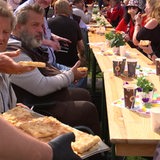 Mehrere Menschen auf Bierbänken essen Butterkuchen und trinken Kaffee.