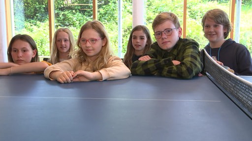 Sechs Kinder stehen vor einer Tischtennisplatte. 