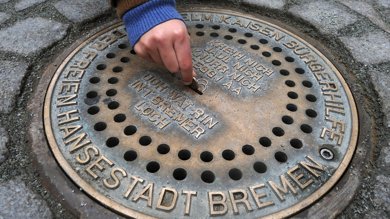 Eine Hand steckt eine Münze in einen Gullydeckel