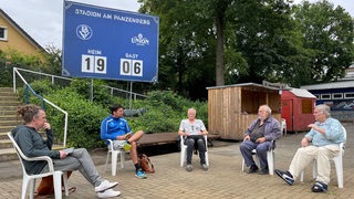 Die Vereinsverantwortlichen des Bremer SV sitzen mit Abstand am Rande des Stadions am Panzenberg bei einer Besprechung.