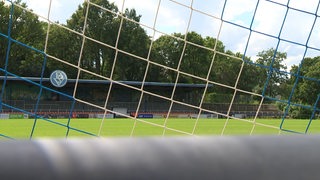 Zu sehen ist das Stadion am Panzenberg aus der Perspektive hinter dem Tor mit Blick durch das Tornetz auf die Haupttribüne.