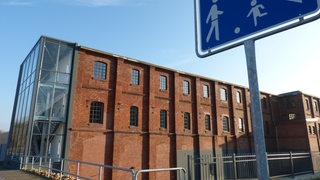 Ein Spielstraßenschild steht vor einem alten Industriegebäude.