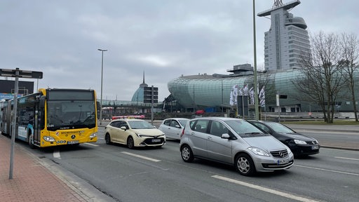 Bus und Pkw fahren auf einer Straße, im Hintergrund das Klimahaus und das Atlantic-Hotel.