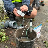 Zwei Hände halten technisches Gerät neben einer Grünfläche.